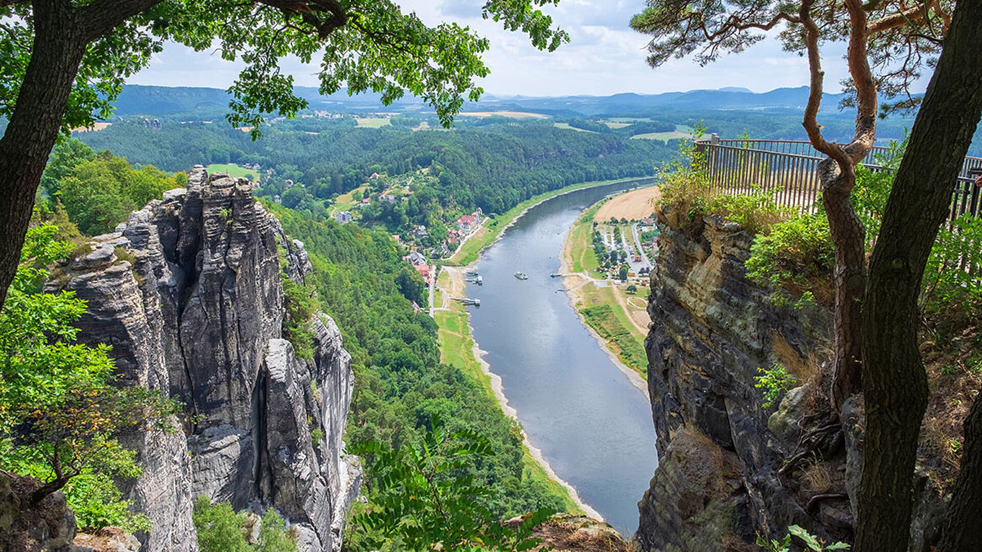 © fotografci - AdobeStock.com Aussicht von Felsen auf die Elbe in der Sächsischen Schweiz mit grünem Tal und Dorf im Sommer