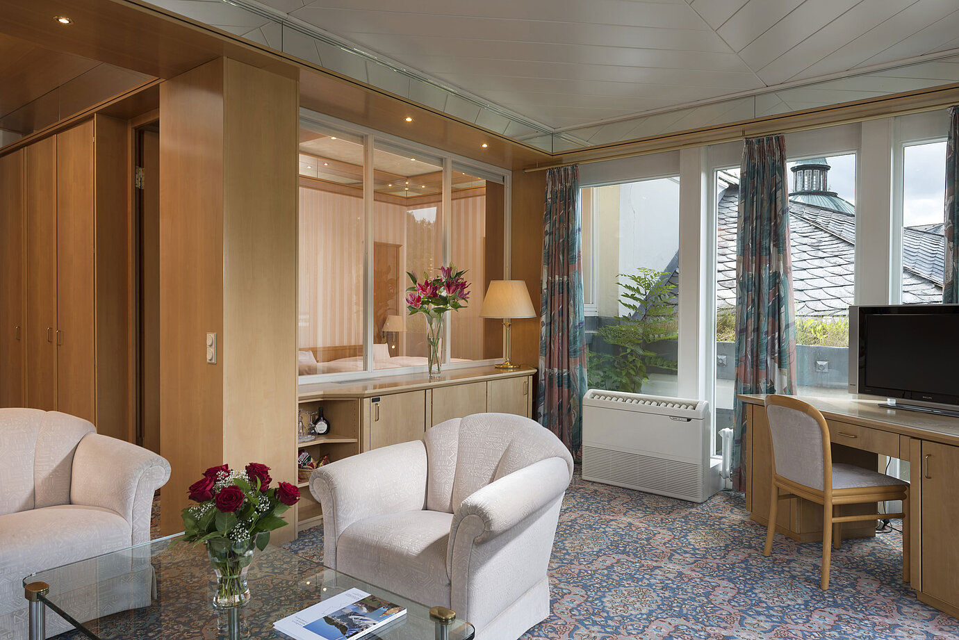 Stilvoller Wohnraum mit Sesseln, TV, Fensterfront und Blick auf das Dach im Maritim Hotel Bad Wildungen