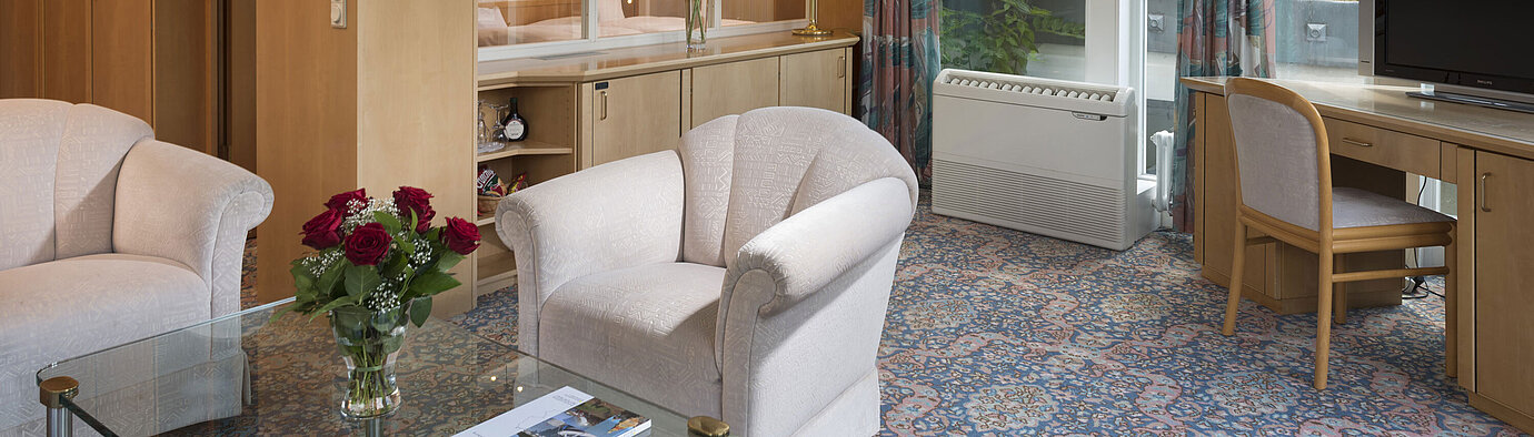 Stilvoller Wohnraum mit Sesseln, TV, Fensterfront und Blick auf das Dach im Maritim Hotel Bad Wildungen