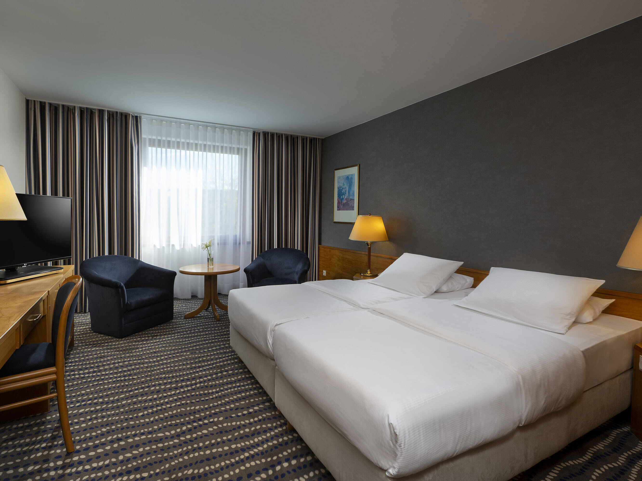 Hotelzimmer mit Doppelbett, TV, Schreibtisch und gemütlicher Sitzecke, ideal für Erholung und Komfort