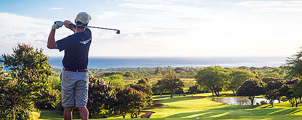 Golfer beim Abschlag auf einem sonnigen Golfplatz mit Blick über das gepflegte Fairway und die Landschaft.