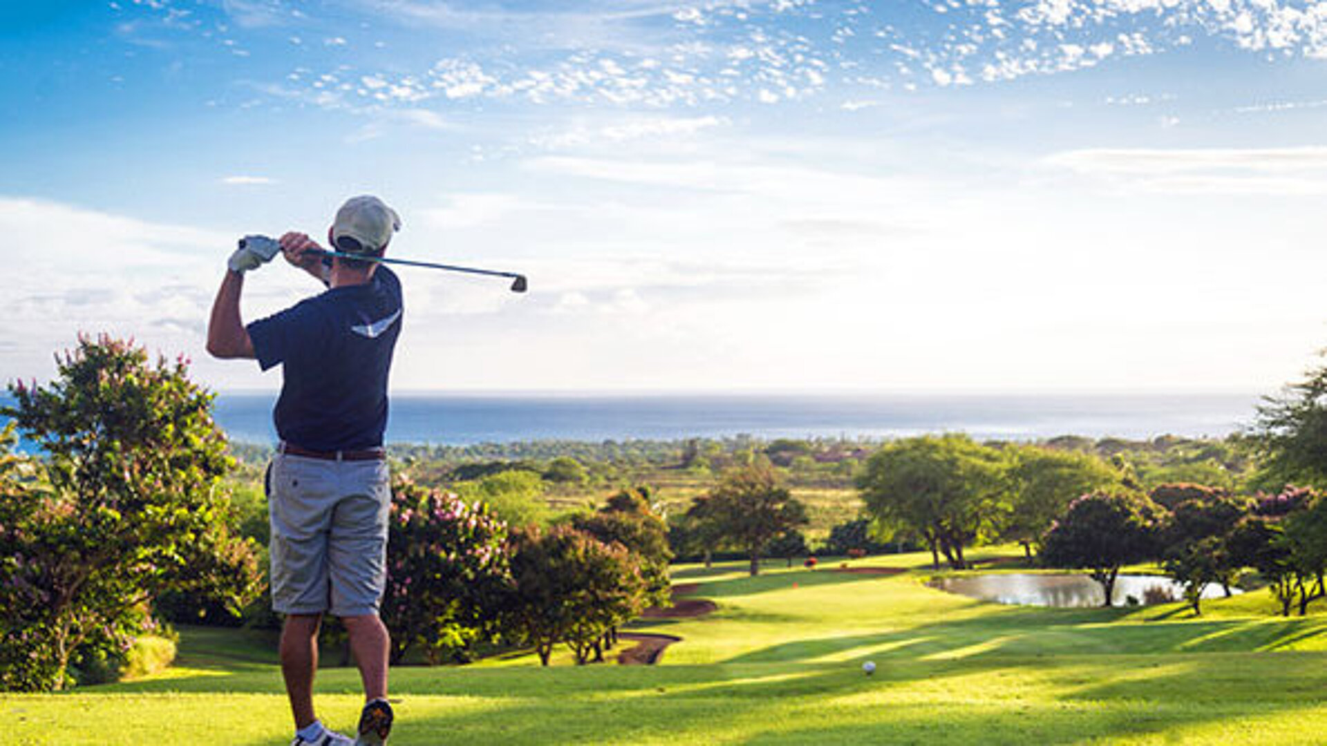 © Allen.G - AdobeStock.com Golfer beim Abschlag auf einem sonnigen Golfplatz mit Blick über das gepflegte Fairway und die Landschaft.