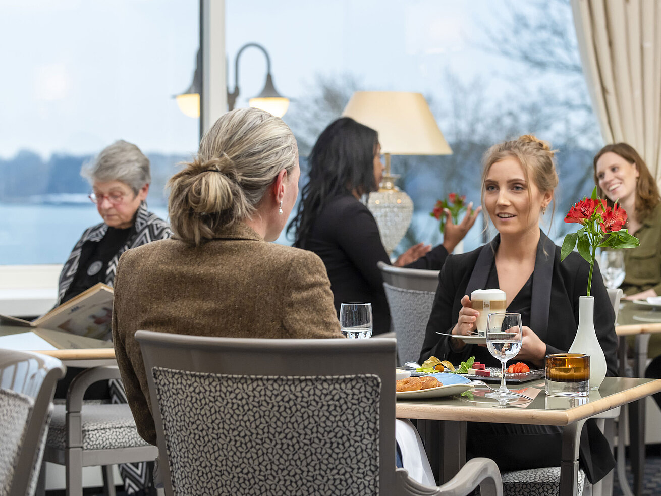 Gäste im Restaurant Bellevue im Maritim Hotel Kiel, entspannte Gespräche bei Getränken und Speisen mit Blick auf das Meer.