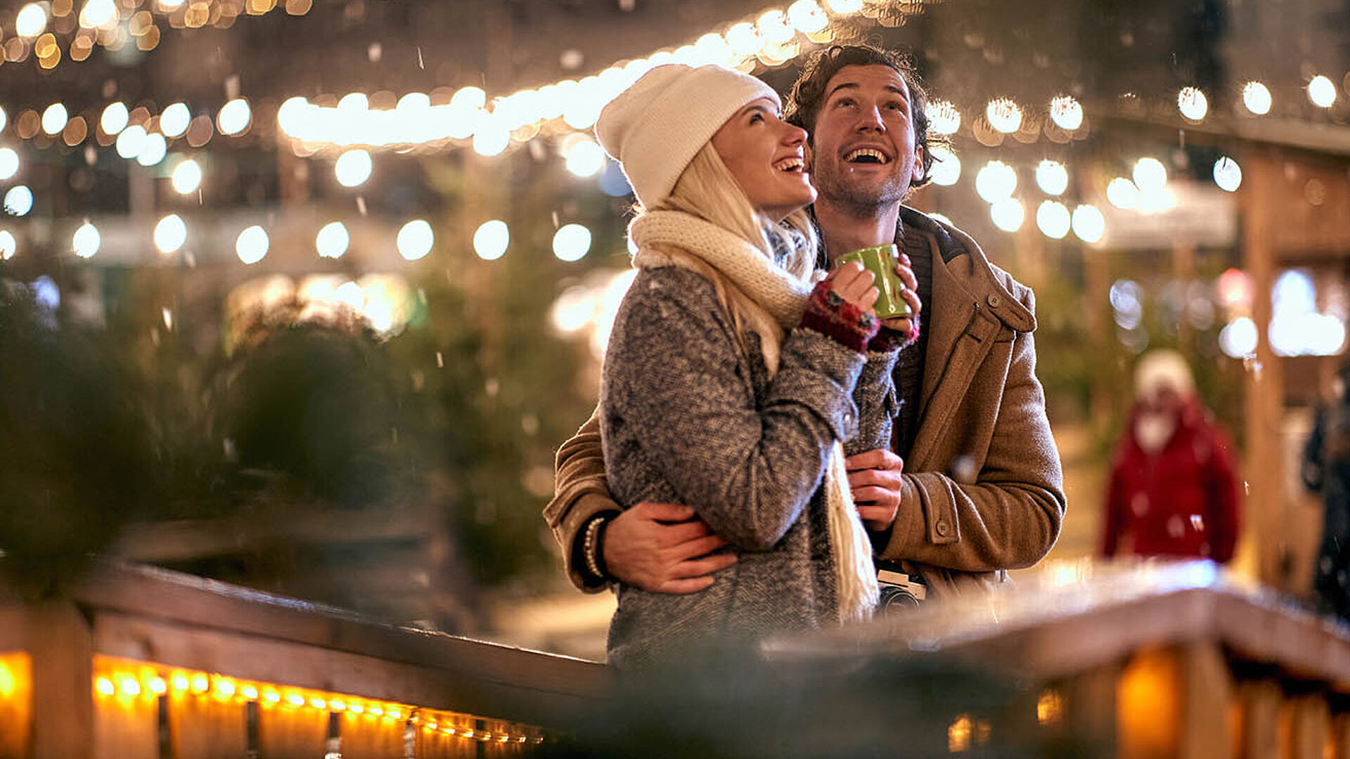 Paar genießt einen winterlichen Abend auf dem Weihnachtsmarkt, umgeben von warmen Lichtern und festlicher Stimmung.