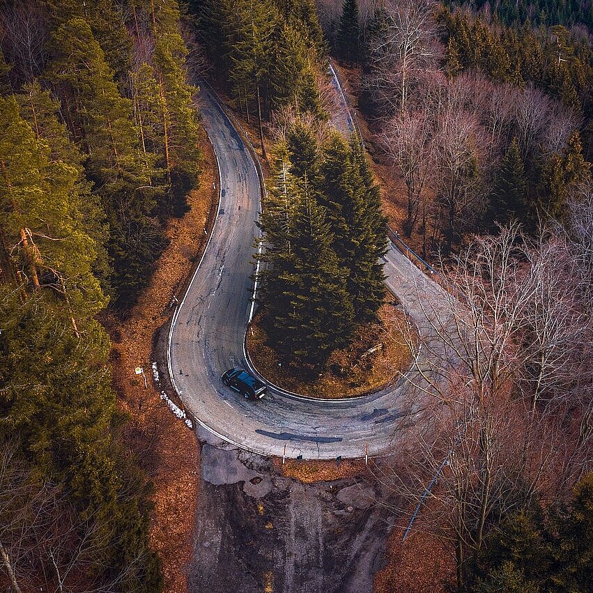 Kurvenreiche Straße durch herbstlichen Wald im Schwarzwald aus der Vogelperspektive.