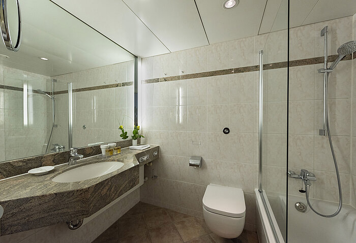 Helles Badezimmer im Maritim Hotel Travemünde mit Granitwaschtisch, Spiegel und Dusche