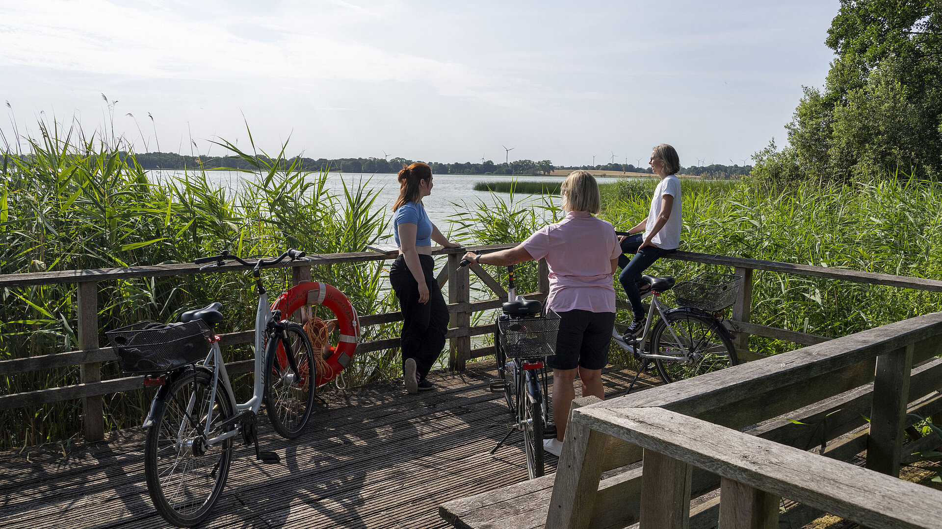 Fahrradtour Drei Frauen machen eine Pause auf einer Fahrradtour an einem Steg mit Blick auf den See beim Maritim Timmendorfer Strand.