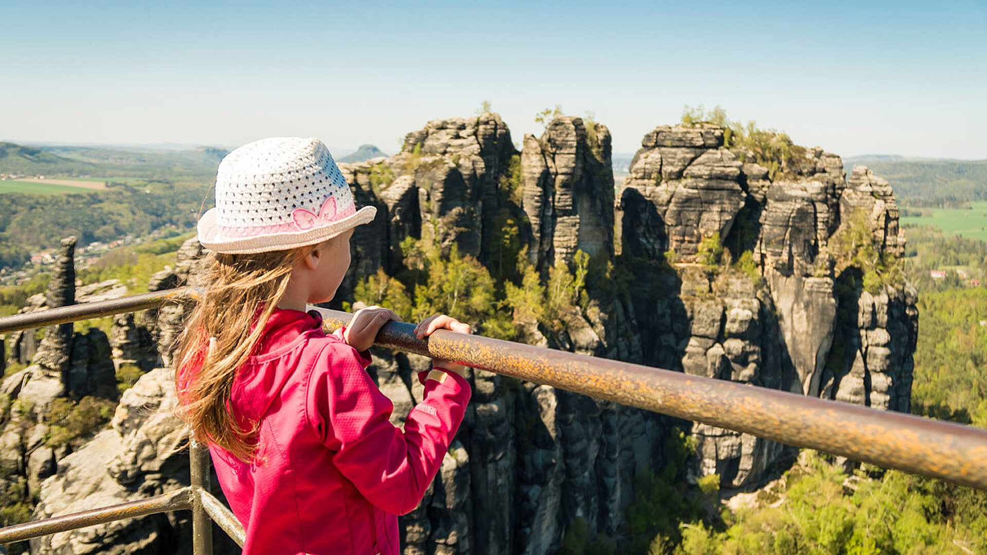 © StockPixstore - AdobeStock.com Kind mit Hut genießt Panoramablick auf Felsenlandschaft der Sächsischen Schweiz bei strahlendem Sonnenschein