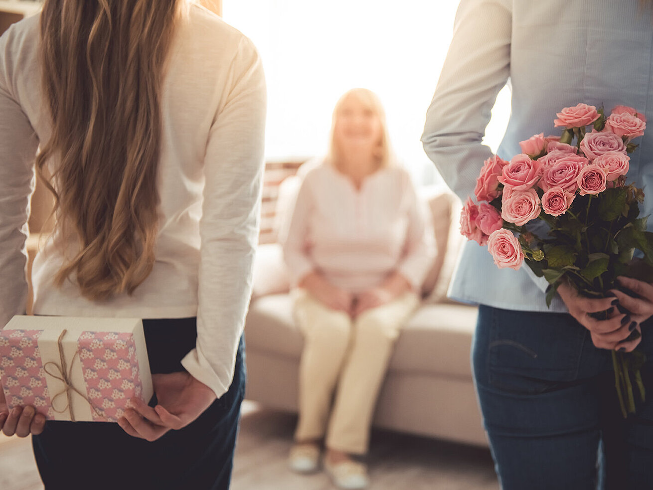 Zwei Töchter überraschen ihre Mutter mit Blumen und Geschenk im Wohnzimmer