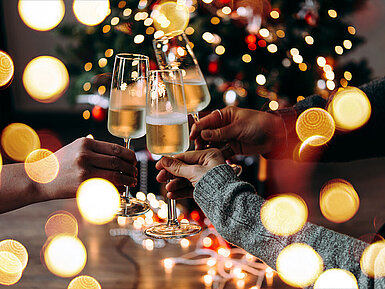 Drei Personen stoßen mit Sektgläsern vor einem festlich beleuchteten Weihnachtsbaum an