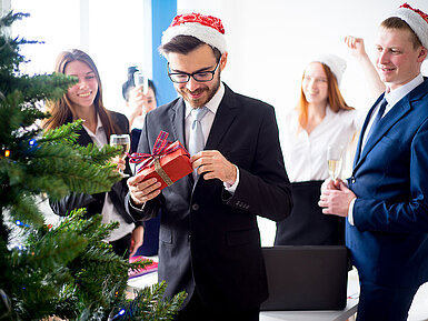 © Nichizhenova Elena - AdobeStock.com Kollegen beschenken sich bei einer Weihnachtsfeier im Hotel