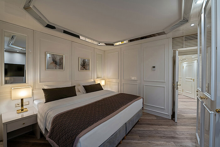 Schlafbereich eines Hotelzimmers mit Doppelbett, Nachttischen, warmem Licht und klassischer Einrichtung.