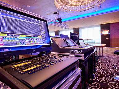 Professionelles Licht- und Mischpult in einem modern ausgestatteten Veranstaltungsraum mit Bühne.