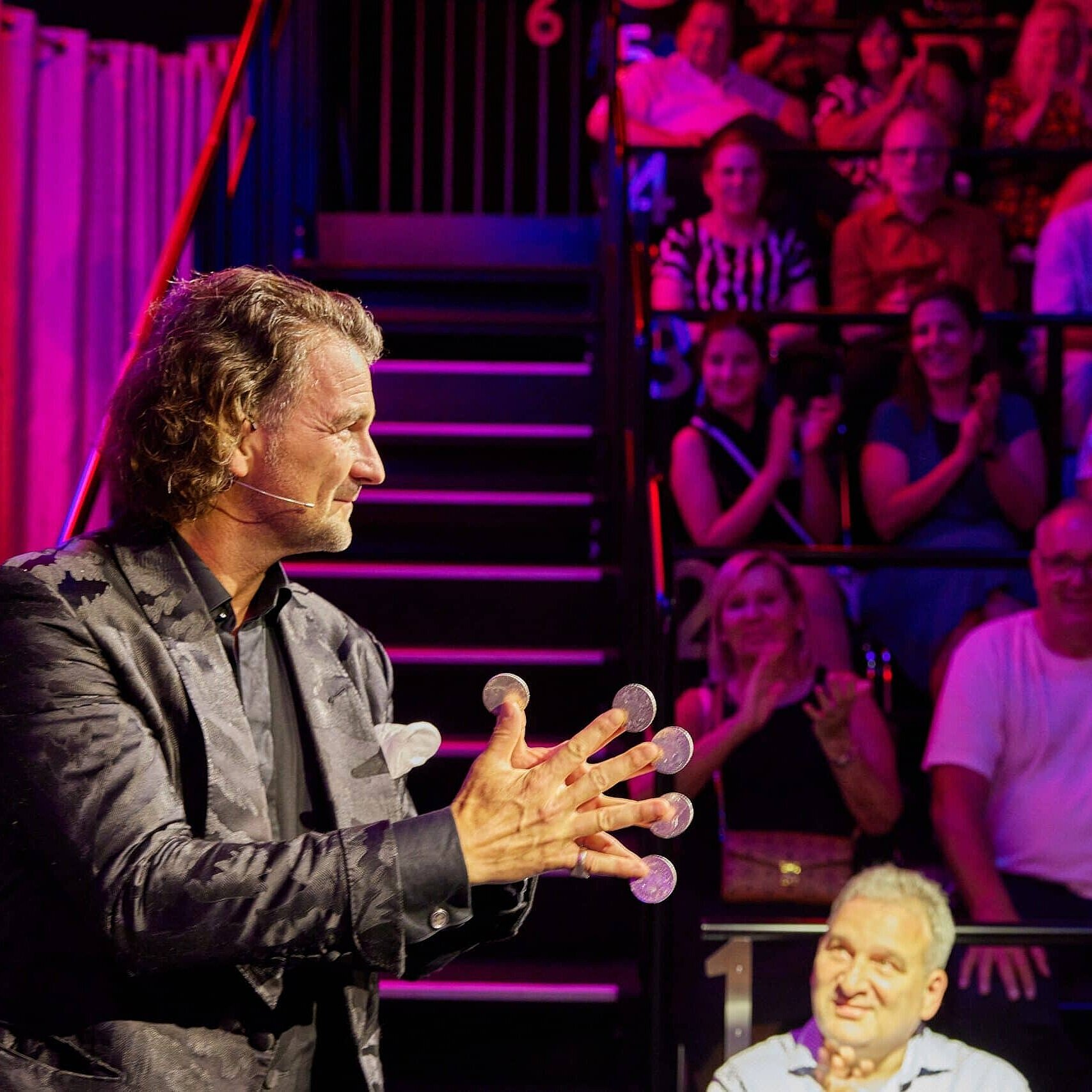 Entertainer bei einer Live-Show vor Publikum in stimmungsvoll beleuchtetem Veranstaltungsraum.