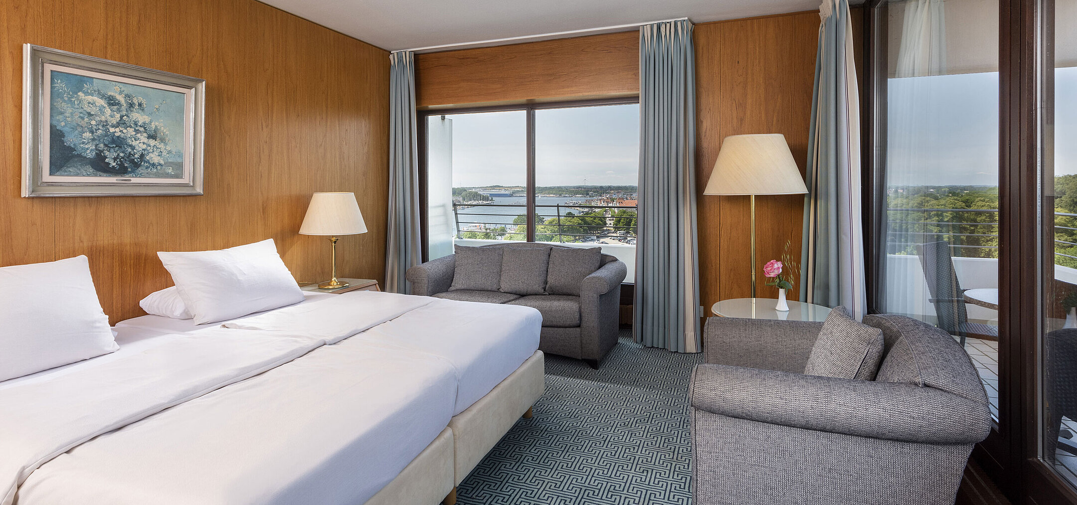 Modernes Doppelzimmer mit gemütlicher Sitzecke und großem Fenster mit Blick auf die Lübecker Bucht