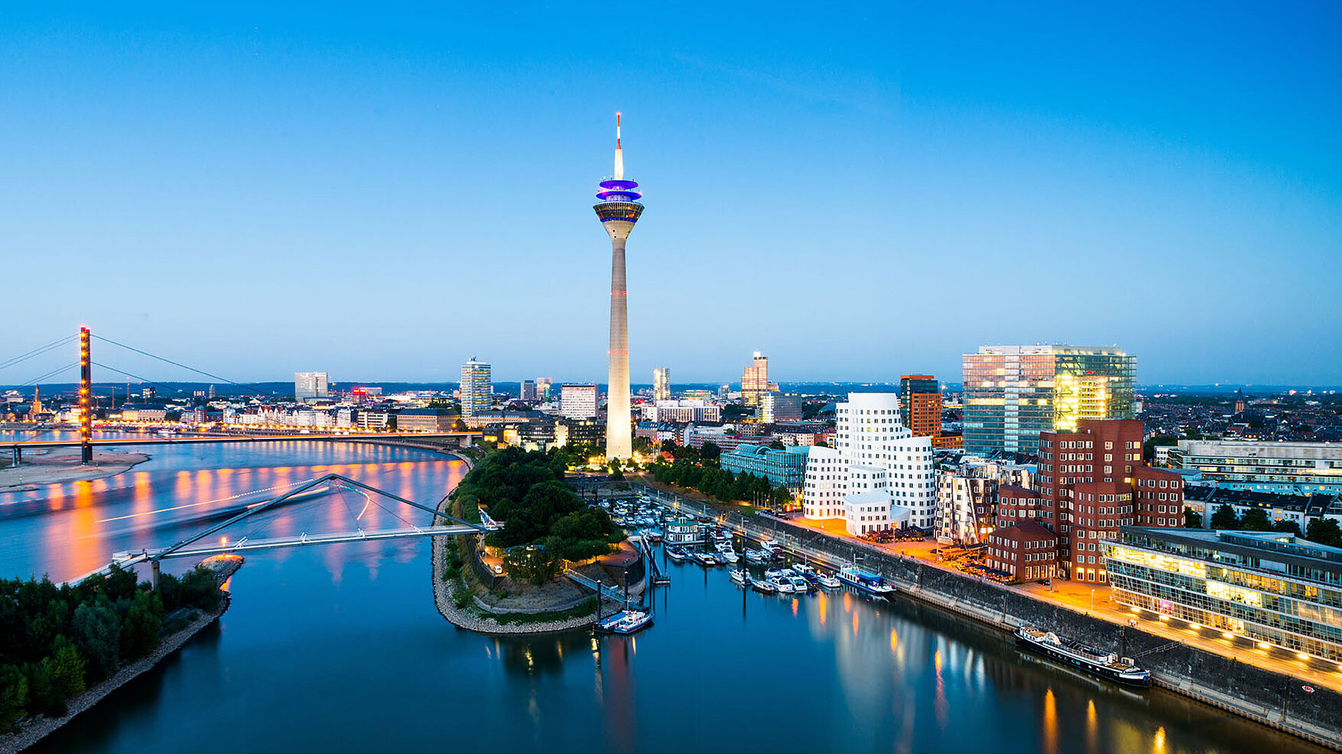 © conorcrowe - AdobeStock.com Düsseldorf Skyline mit Rheinturm, Rheinpromenade und moderner Architektur bei Abenddämmerung.
