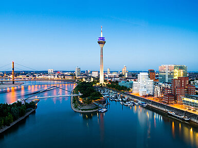 © conorcrowe - AdobeStock.com Düsseldorf Skyline mit Rheinturm, Rheinpromenade und moderner Architektur bei Abenddämmerung.