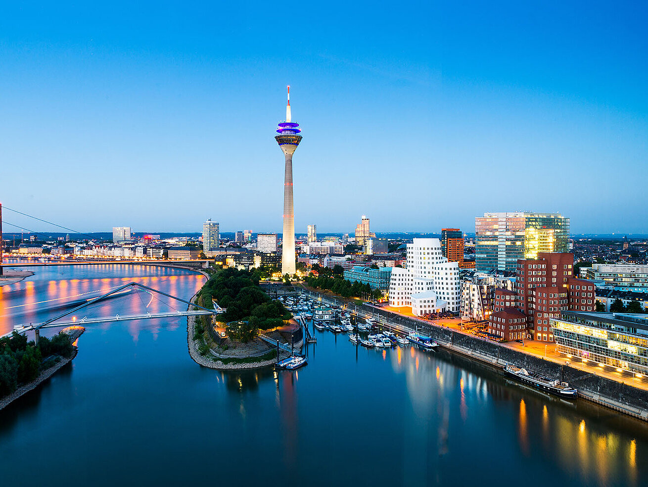 © conorcrowe - AdobeStock.com Düsseldorf Skyline mit Rheinturm, Rheinpromenade und moderner Architektur bei Abenddämmerung.