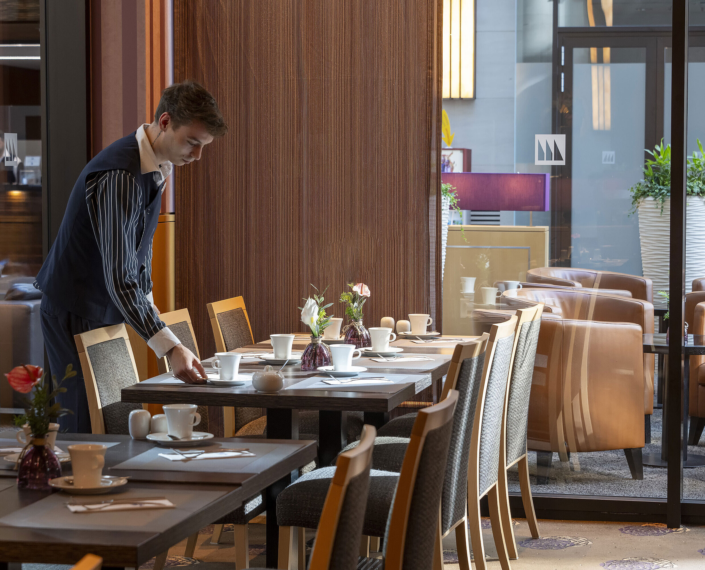 Mitarbeiter deckt einen Tisch im Restaurant Classico des Maritim Hotel Düsseldorf, umgeben von eleganter Einrichtung.