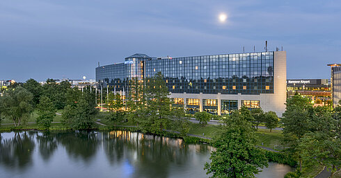 Beleuchtetes Maritim Hotel Hannover mit Glasfassade und Seespiegelung in der Abenddämmerung.