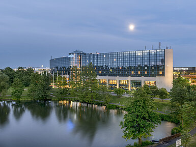 Beleuchtetes Maritim Hotel Hannover mit Glasfassade und Seespiegelung in der Abenddämmerung.