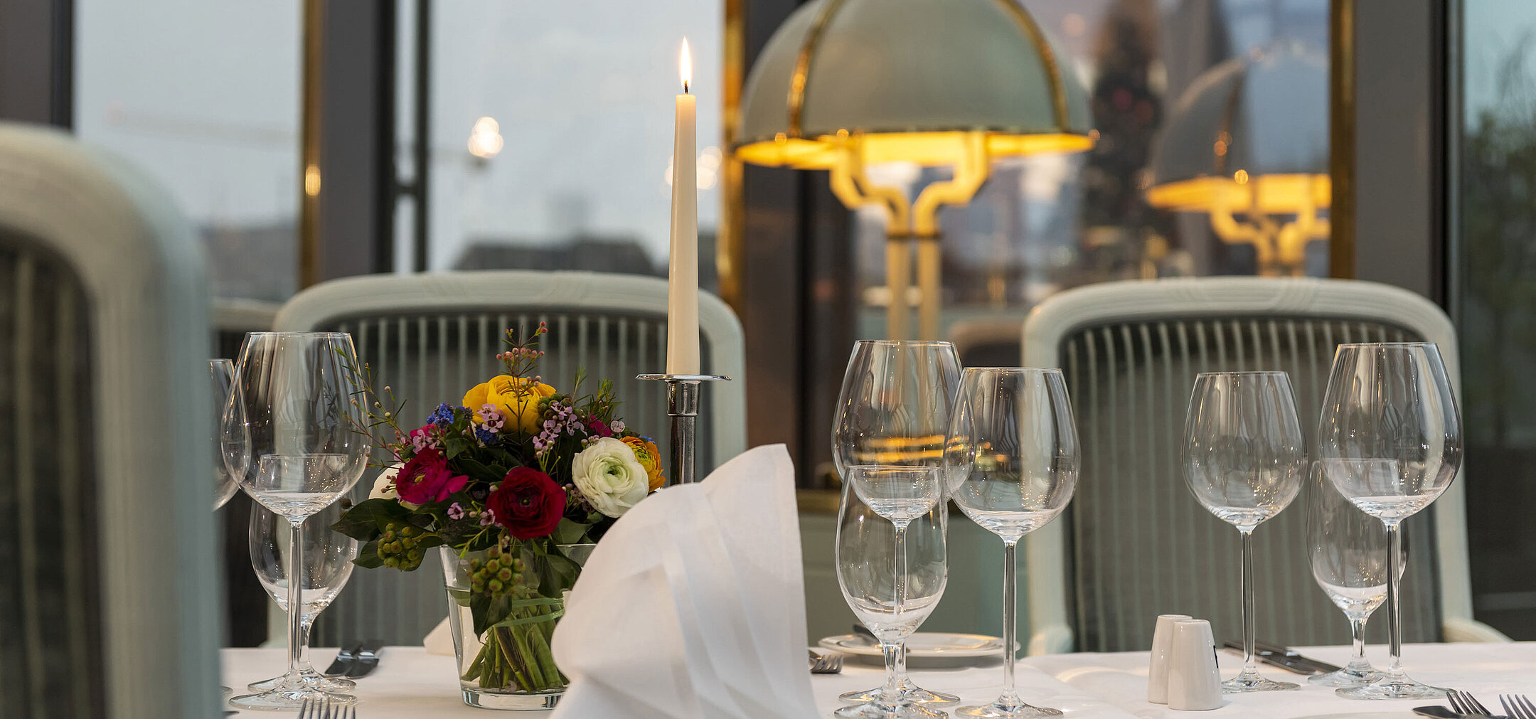 Elegant gedeckter Tisch im Restaurant mit Kerze, Weingläsern und Blumenarrangement, perfekt für ein gehobenes Abendessen.