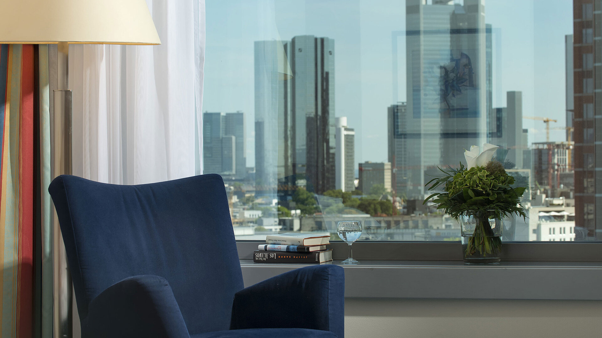 Ausblick auf die Skyline von Frankfurt Ausblick aus einer Suite im Maritim Hotel Frankfurt mit Skyline-Blick, blauem Sessel und dekorativem Blumenarrangement.
