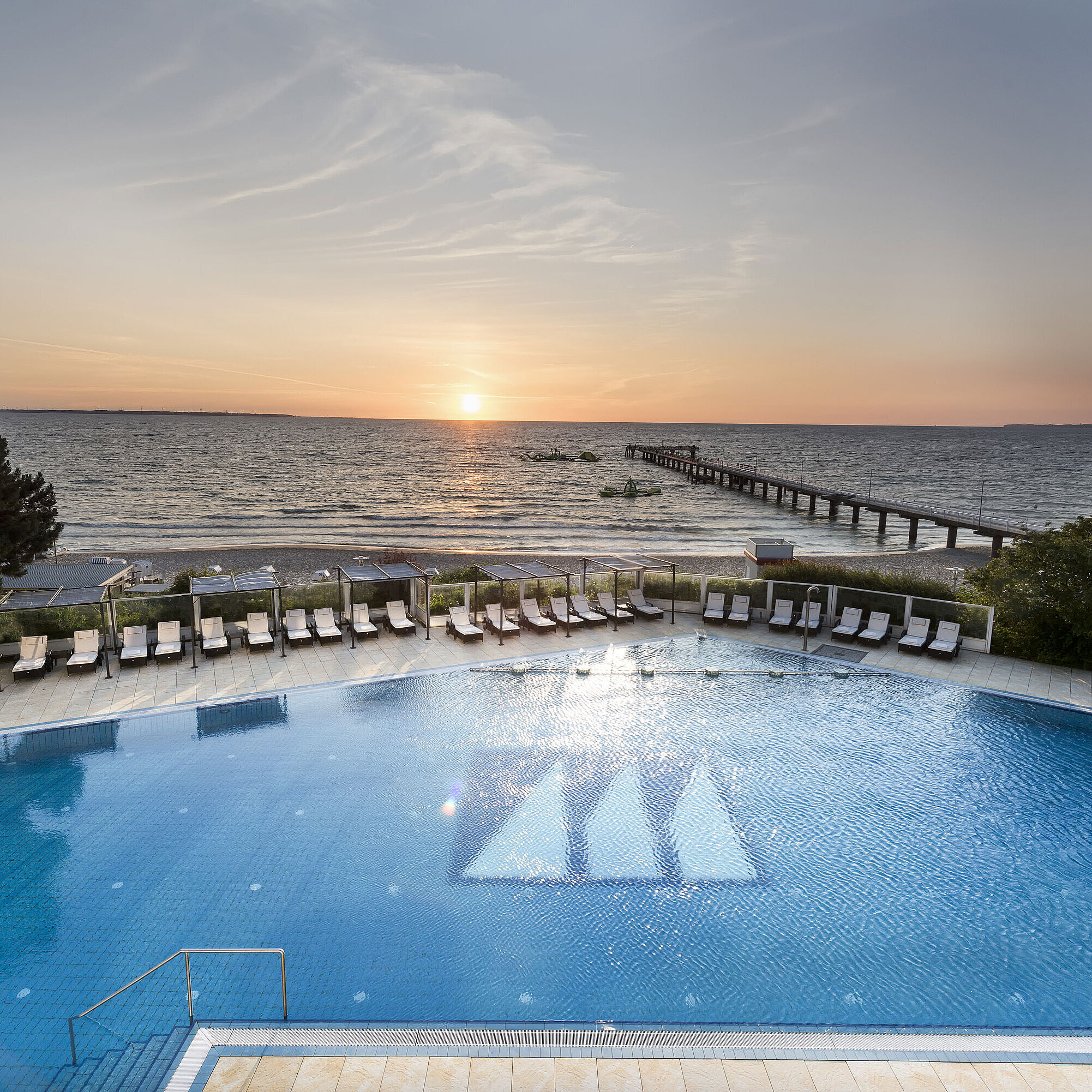 Pool mit Meerblick im Maritim Seehotel Timmendorfer Strand bei Sonnenuntergang, Liegen und Steg am Strand.