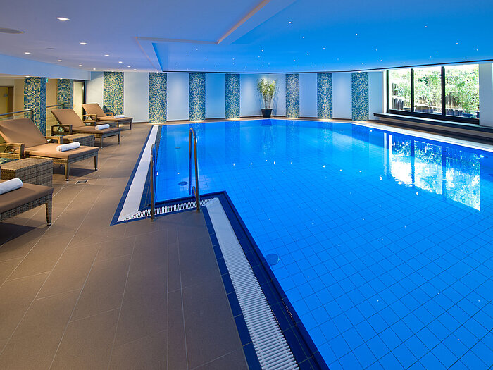 Heller und moderner Innenpool im Maritim Hotel Darmstadt mit Liegestühlen und großen Fenstern mit Blick ins Grüne.