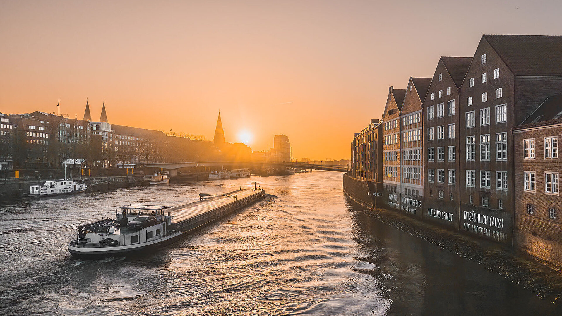 © Timo - AdobeStock.com Bremen an der Weser bei Sonnenuntergang mit historischen Gebäuden am Ufer und Schiffen auf dem Fluss