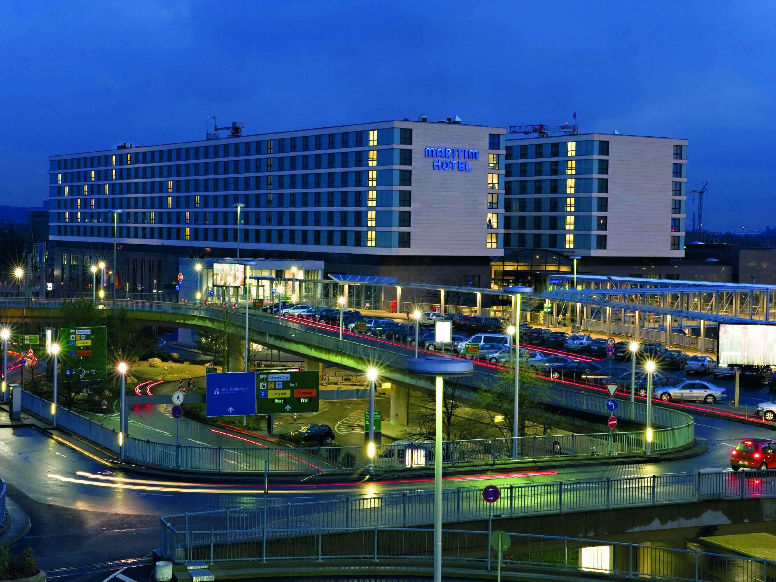 Nachtaufnahme des Maritim Hotel Düsseldorf mit beleuchteter Fassade, direkter Lage am Flughafen und moderner Architektur.
