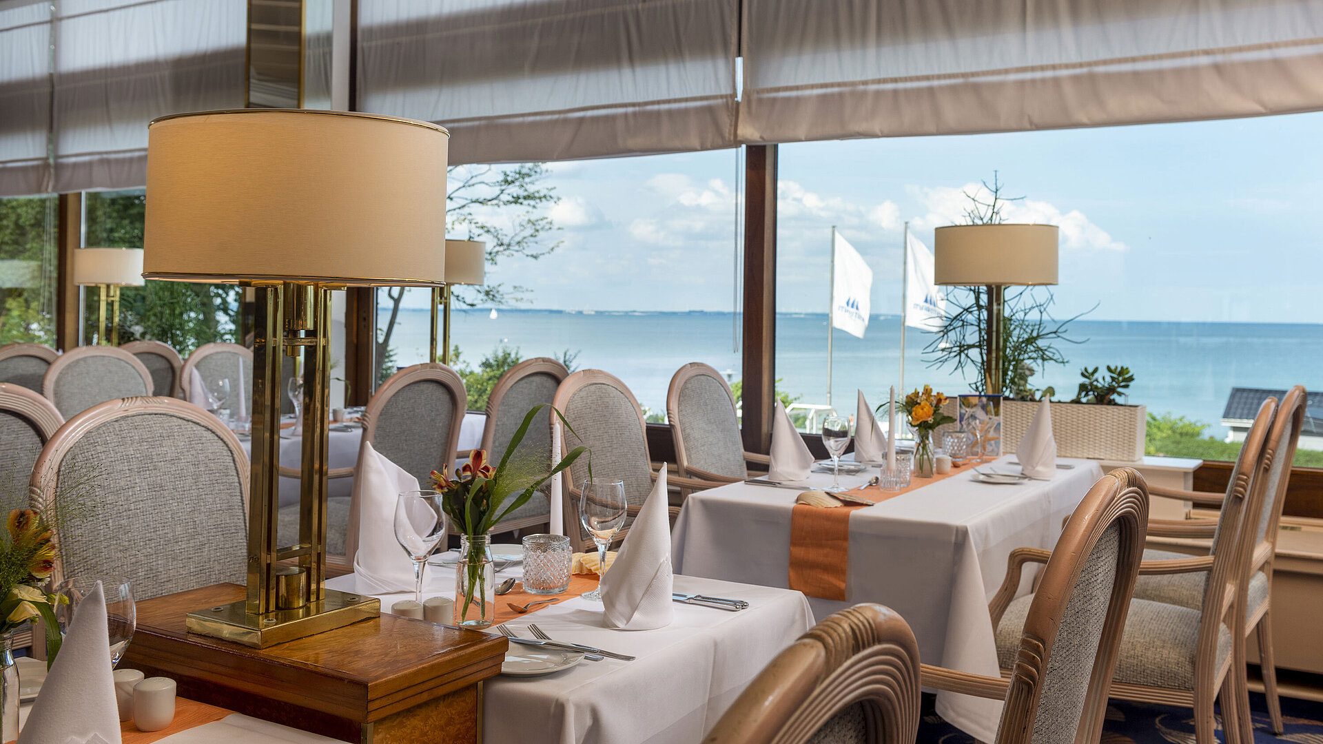 Restaurant Elegantes Restaurant mit gedeckten Tischen und Meerblick, dekoriert mit Lampen und Blumen für ein gehobenes Speiseerlebnis.