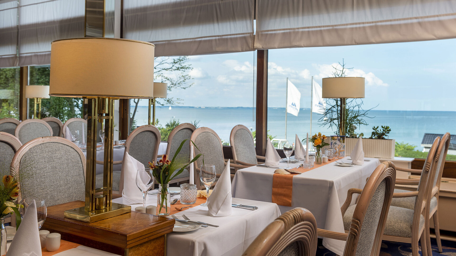 Elegantes Restaurant mit gedeckten Tischen und Meerblick, dekoriert mit Lampen und Blumen für ein gehobenes Speiseerlebnis.