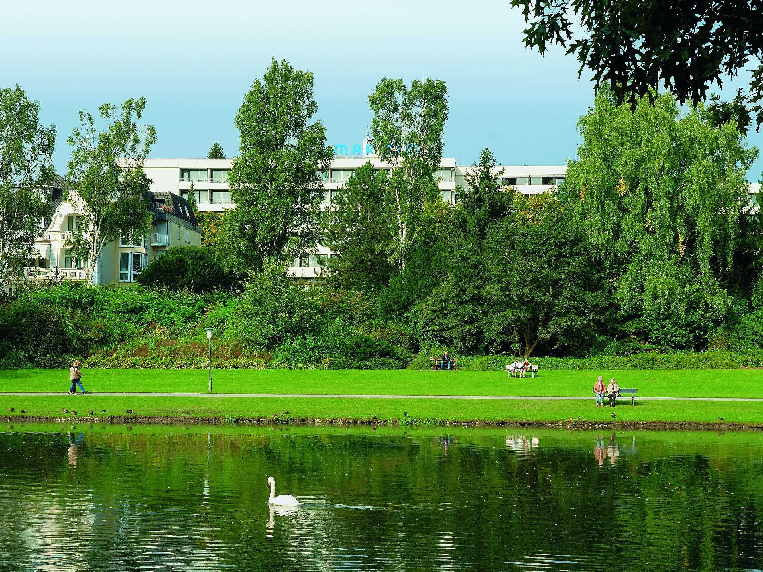Blick auf das Maritim Hotel Bad Salzuflen hinter dem grünen Kurpark mit See und Schwan