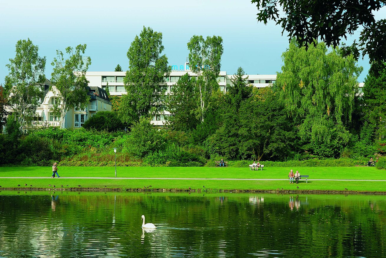 Blick auf das Maritim Hotel Bad Salzuflen hinter dem grünen Kurpark mit See und Schwan