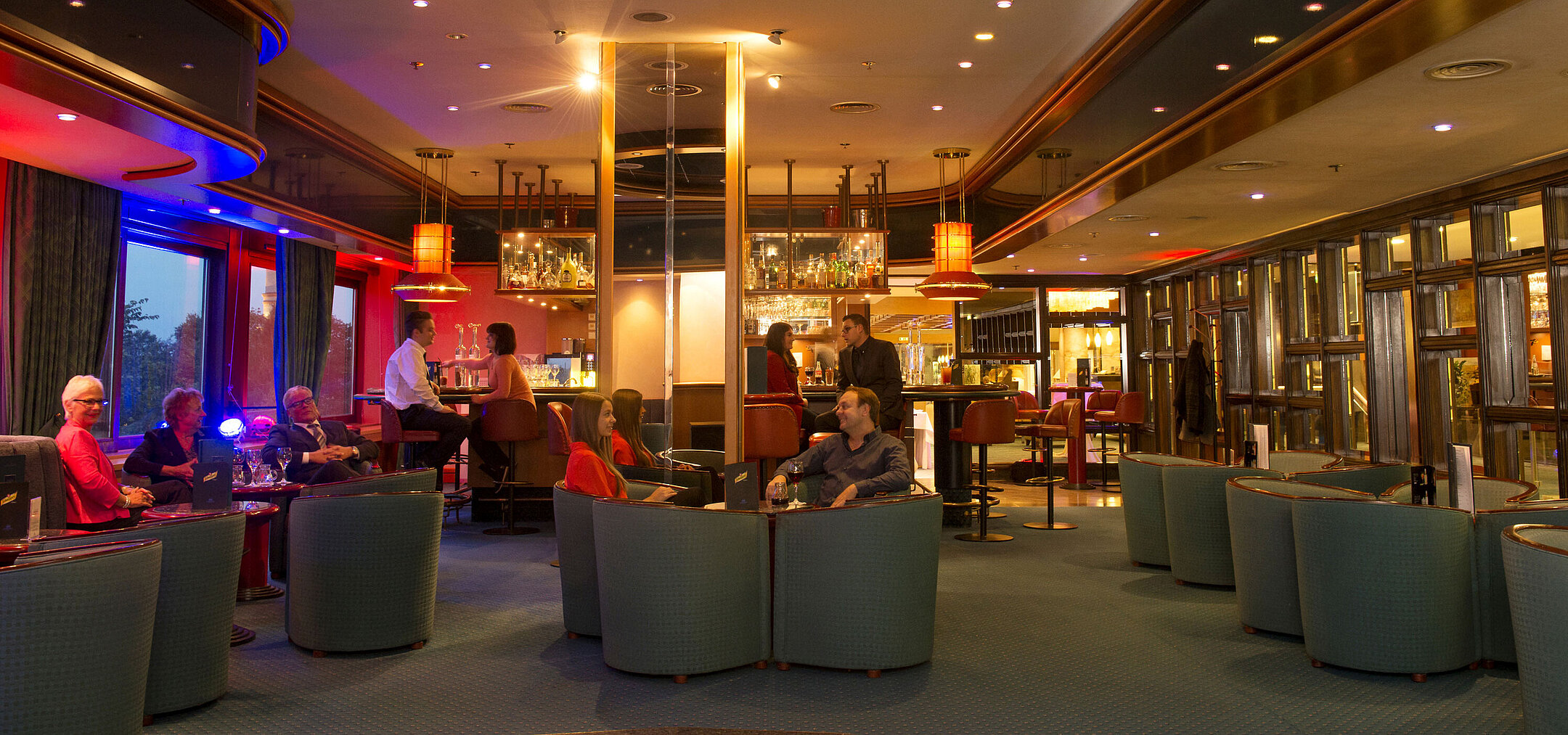Gäste genießen Drinks und Gespräche in der stilvollen Bar des Maritim Hotel Travemünde bei Abendstimmung