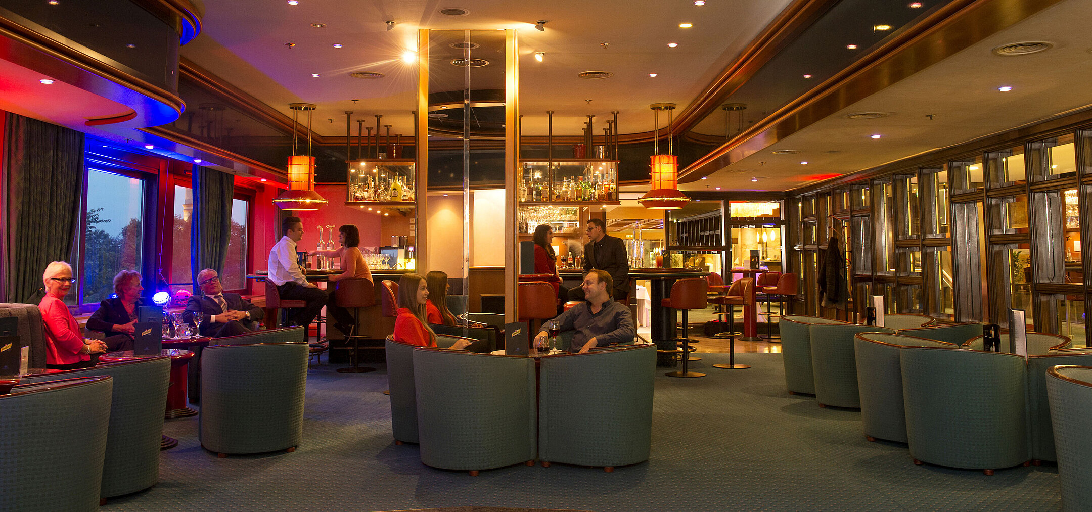 Gäste genießen Drinks und Gespräche in der stilvollen Bar des Maritim Hotel Travemünde bei Abendstimmung