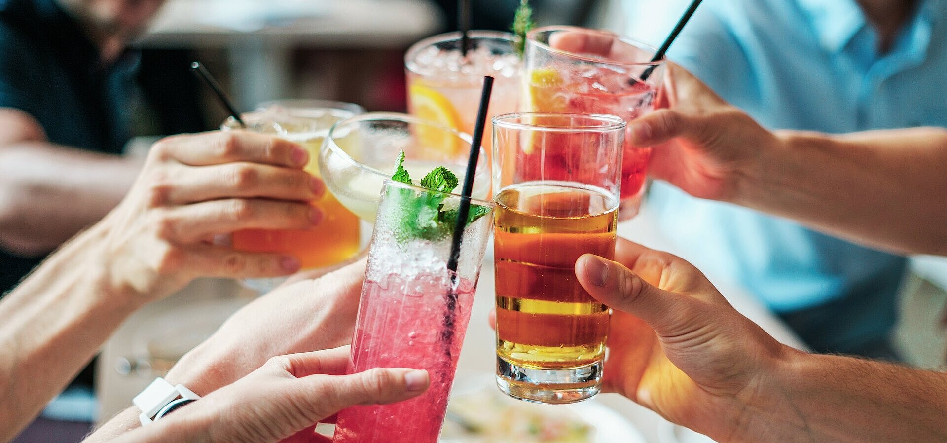 Mehrere Personen stoßen mit bunten Getränken und Cocktails in Gläsern bei geselligem Beisammensein an.