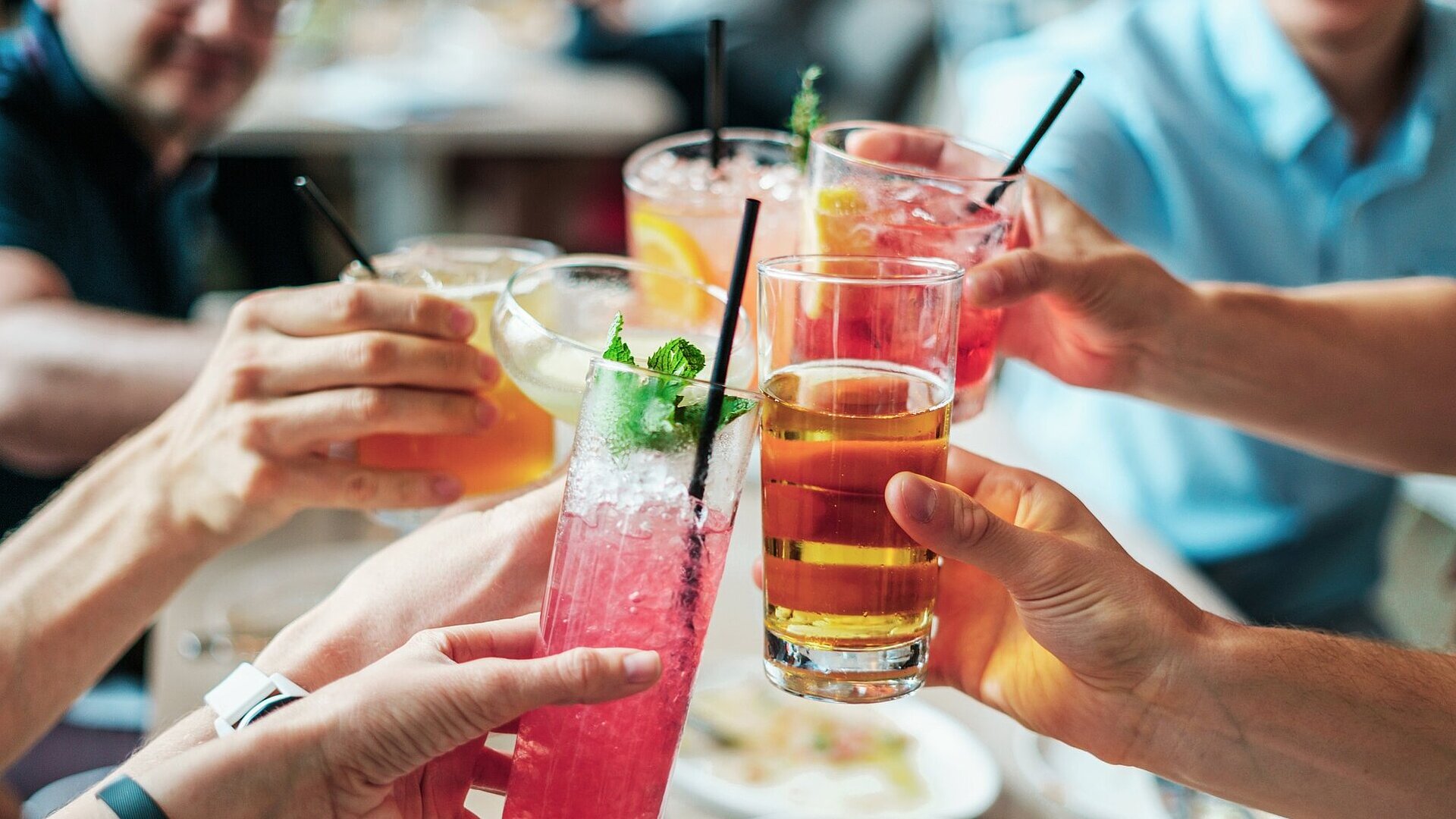 Gemeinsamer Anstoß mit Getränken Mehrere Personen stoßen mit bunten Getränken und Cocktails in Gläsern bei geselligem Beisammensein an.