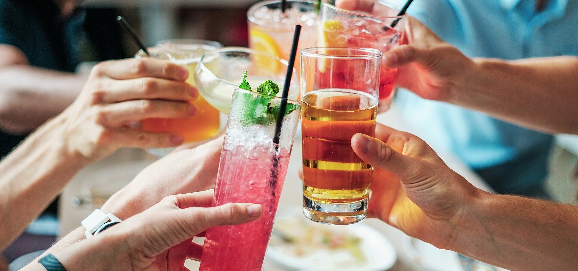 Mehrere Personen stoßen mit bunten Getränken und Cocktails in Gläsern bei geselligem Beisammensein an.