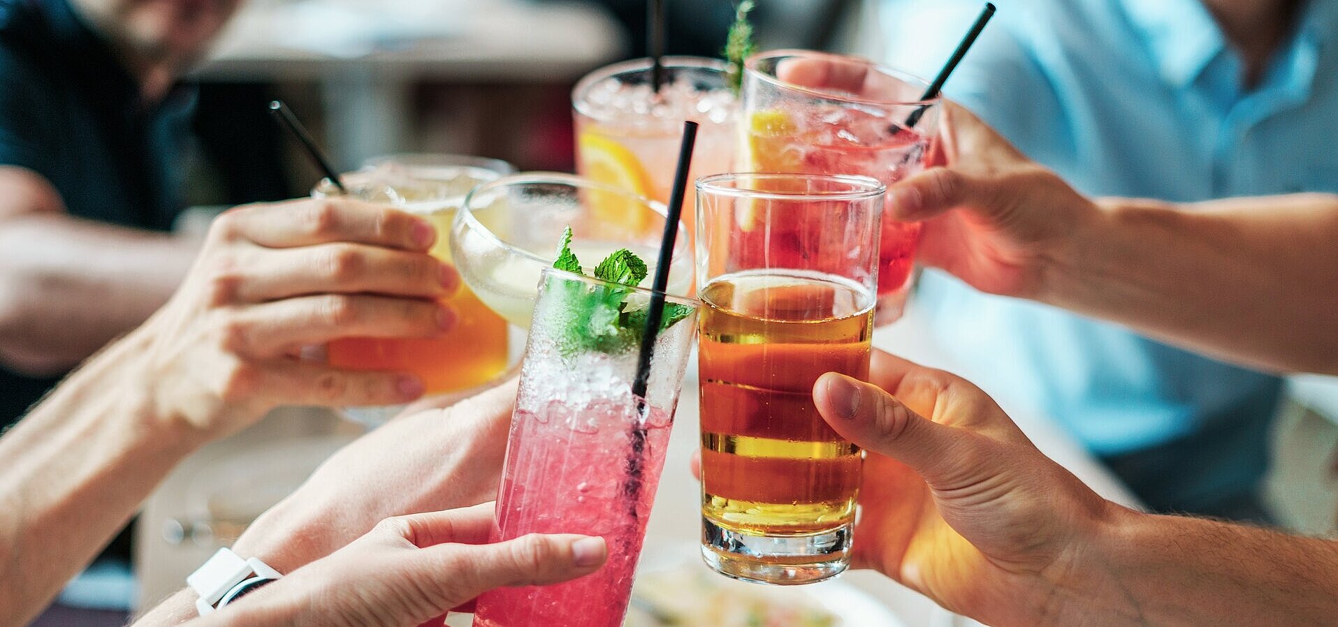 Gemeinsamer Anstoß mit Getränken Mehrere Personen stoßen mit bunten Getränken und Cocktails in Gläsern bei geselligem Beisammensein an.