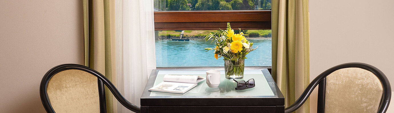 Tisch mit Sitzgelegenheiten am Fenster der Junior Suite im Maritim Hotel Königswinter mit Blick auf den Rhein.