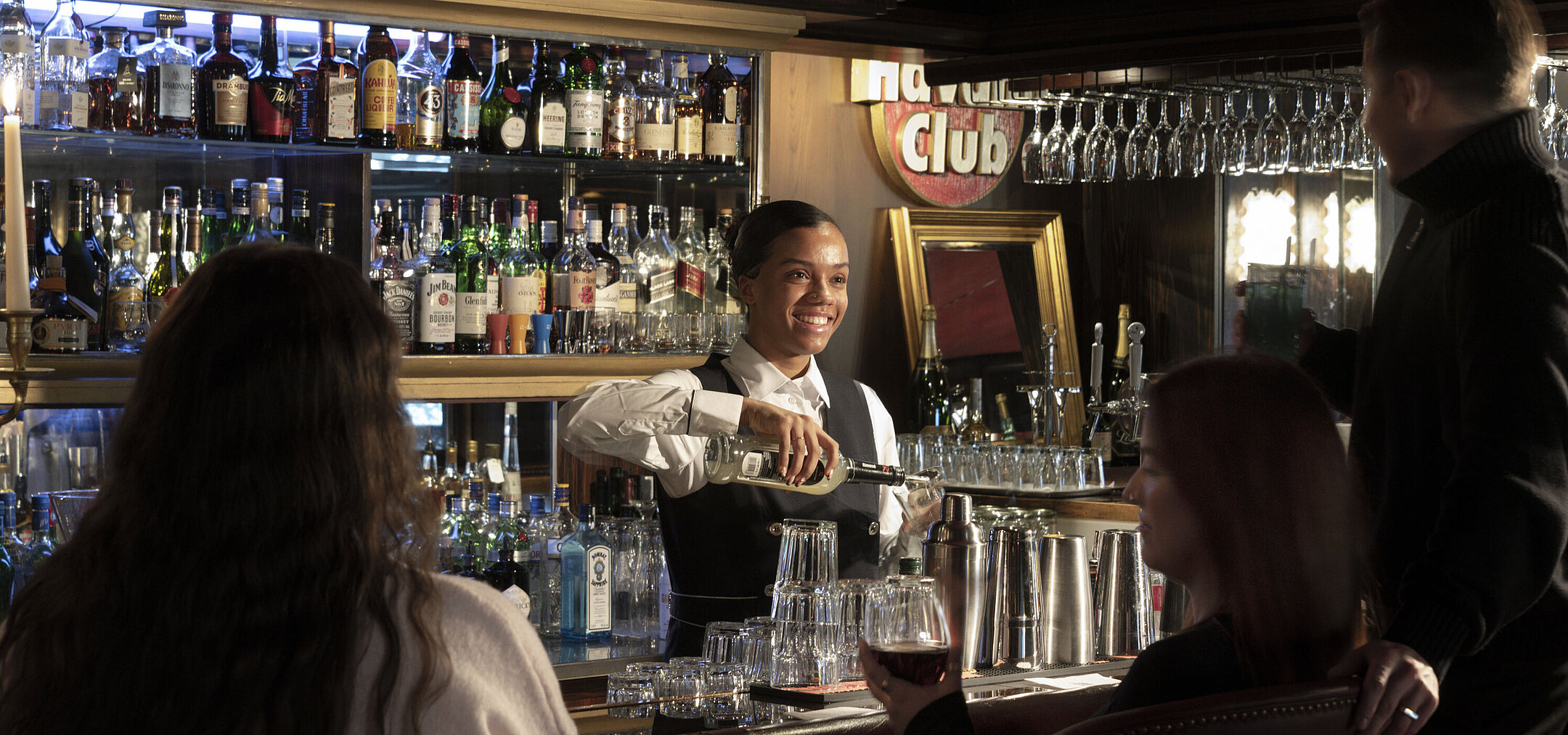 Bartenderin an der stilvollen Bar im Maritim Hotel Kiel serviert Getränke mit freundlichem Lächeln und einladender Atmosphäre.