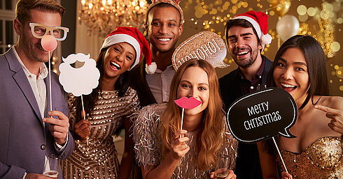 © Monkey Business - AdobeStock.com Elegante Gruppe bei festlicher Weihnachtsfeier mit Sekt und Weihnachtsmützen vor goldenem Hintergrund