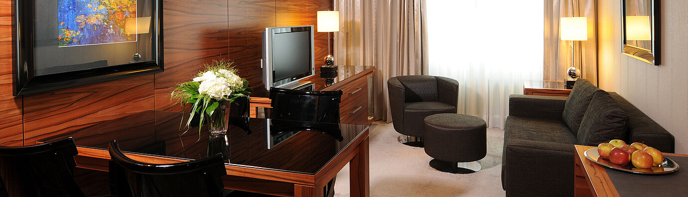 Junior Suite Heller Wohnbereich mit Sofa, Sessel, TV und Schreibtisch im Maritim Hotel München