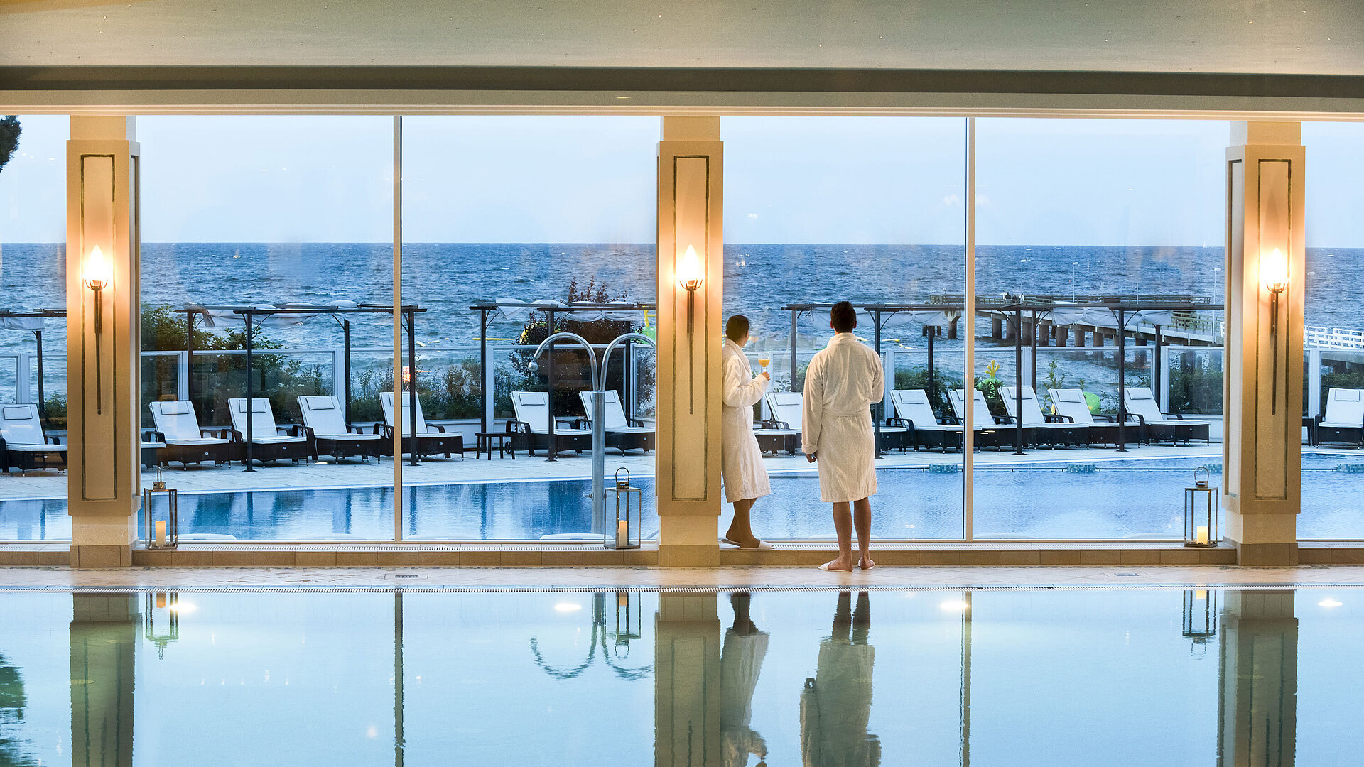 Innenpool mit Meerblick im Maritim Seehotel Timmendorfer Strand, zwei Gäste in Bademänteln am Fenster.