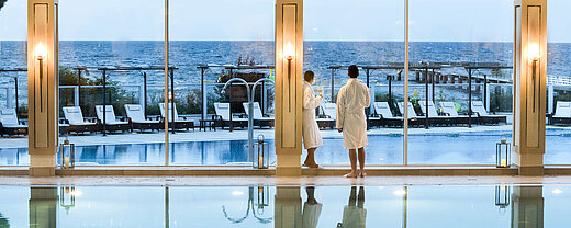 Innenpool mit Meerblick im Maritim Seehotel Timmendorfer Strand, zwei Gäste in Bademänteln am Fenster.