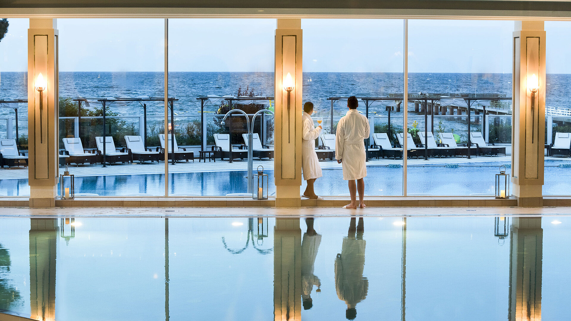 Innenpool mit Meerblick im Maritim Seehotel Timmendorfer Strand, zwei Gäste in Bademänteln am Fenster.