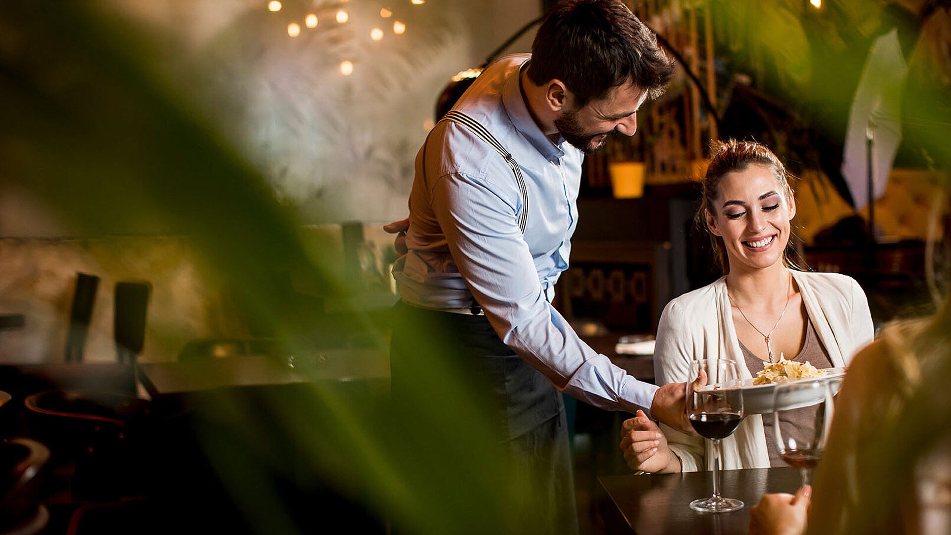 ® BGStock72 - AdobeStock.com Servicemitarbeiter schenkt einer Gästin in stilvoller Restaurantatmosphäre ein Getränk ein.
