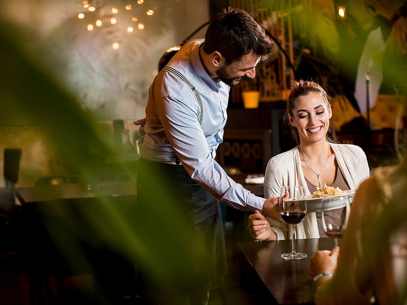 ® BGStock72 - AdobeStock.com Servicemitarbeiter schenkt einer Gästin in stilvoller Restaurantatmosphäre ein Getränk ein.